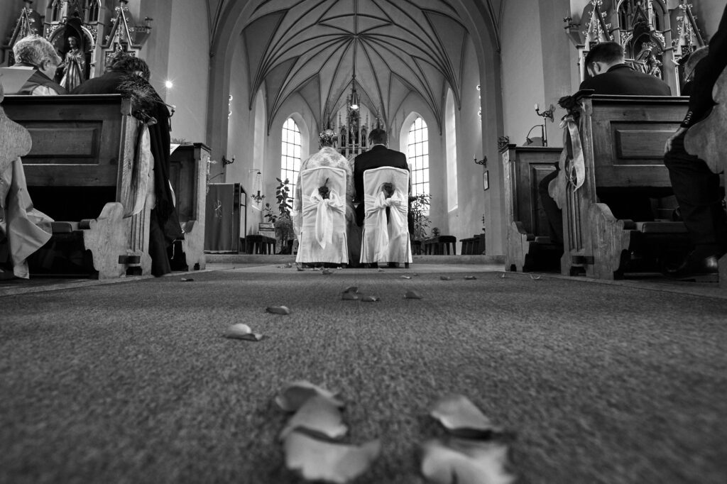 Hochzeitsbilder Ideen: Das Brautpaar vor dem Altar vom Boden aus fotografiert, auf dem Rosenblätter liegen